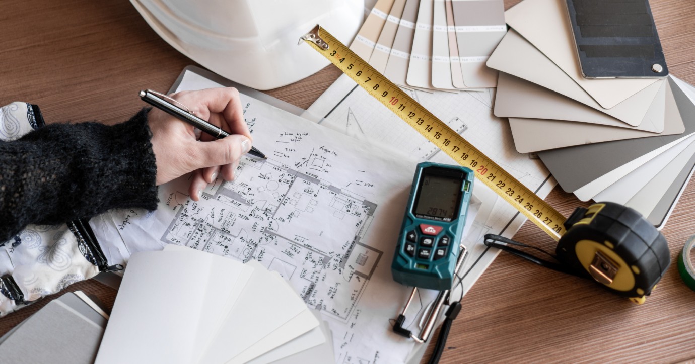 Professionnel annotant un plan avec des outils de mesure pour la conception et l’aménagement d’un bâtiment
